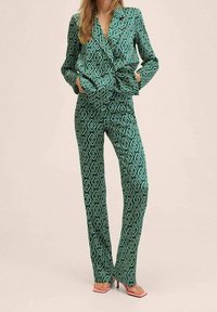 Costume vert à motifs avec une veste ajustée et un pantalon droit, présentant un motif de chaîne en blanc. Texture lisse, silhouette moderne.