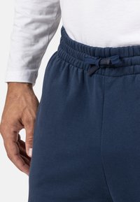 Marineblaue Sweatpants mit elastischem Bund und Kordelzug; glatte Textur; seitliche Tasche; teilweise sichtbares weißes Langarmshirt.