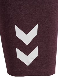 Burgundy träningsshorts i mjukt tyg med tre vita chevron-mönster nära fållen. Horisontell struktur synlig på materialet.