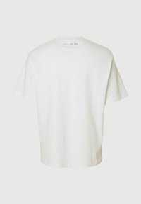 Biała bawełniana koszulka z krótkim rękawem i luźnym krojem. Tył posiada małą nadrukowaną metkę w pobliżu dekoltu.