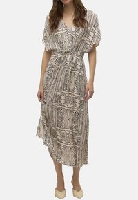 Beige mekko, jossa on kuvioitu muotoilu, lyhyet lepattelevat hihat, vyötärön kiristysnyöri ja epäsymmetrinen helma. Yhdistetty teräväkärkisiin beigeihin kenkiin.