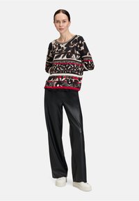 Top a maniche lunghe con motivo in nero, beige e rosso, caratterizzato da disegni floreali e geometrici; abbinato a pantaloni ampi neri in pelle sintetica.