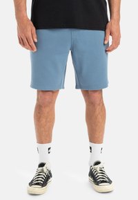 Heldblauwe sportshorts van een katoenmix, met een relaxte pasvorm, een zachte textuur en zijnaad, gedragen met zwarte sneakers en witte sokken.