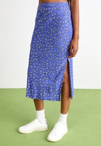 Jupe midi bleu à motif floral avec une fente latérale, en tissu léger. Stylée avec des baskets blanches et des chaussettes côtelées.