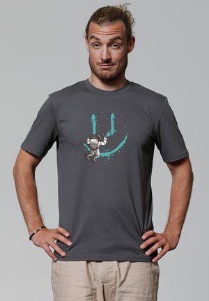 Grijze katoenen T-shirt met een grafiek van een astronaut met een rugzak, die springt tegen een teal spetterachtergrond, ronde hals, korte mouwen.