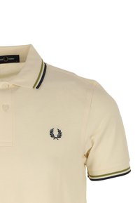 Polo en crème avec un col rayé noir et vert. Présente un petit logo marine sur la poitrine et une patte de boutonnage. Matière en coton.