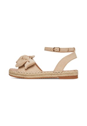 Sandales en daim beige avec un détail de nœud noué, bride de cheville avec boucle, et semelle en jute tressé. Design plat pour le confort.