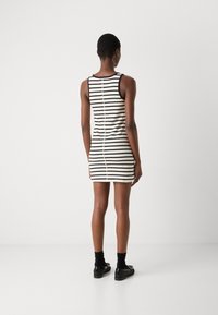 Striped sleeveless dress in white and black, featuring a fitted shape, smooth texture, and a vertical seam detail along the back.