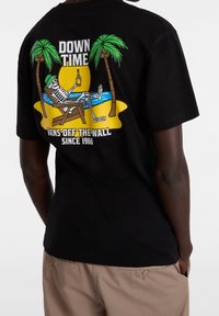 Camiseta de algodón negra con un gráfico colorido de un esqueleto en una silla de playa, palmeras y el texto "DOWN TIME" y "VANS OFF THE WALL."