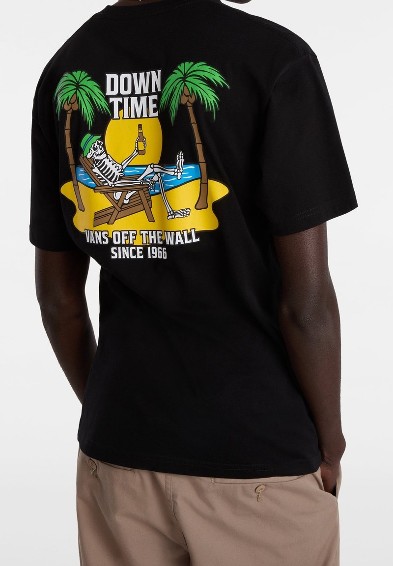 Camiseta de algodón negra con un gráfico colorido de un esqueleto en una silla de playa, palmeras y el texto "DOWN TIME" y "VANS OFF THE WALL."