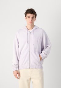 Hanorac cu fermoar de culoare violet deschis, cu un logo brodat, glugă cu șnur și manșete și tiv elastic. Țesătură moale cu o croială lejeră.