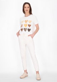 Hvid bomulds t-shirt med et hjerteprint i nuancer af brunt, parret med lysebeige tapered bukser og kridhvide sneakers.
