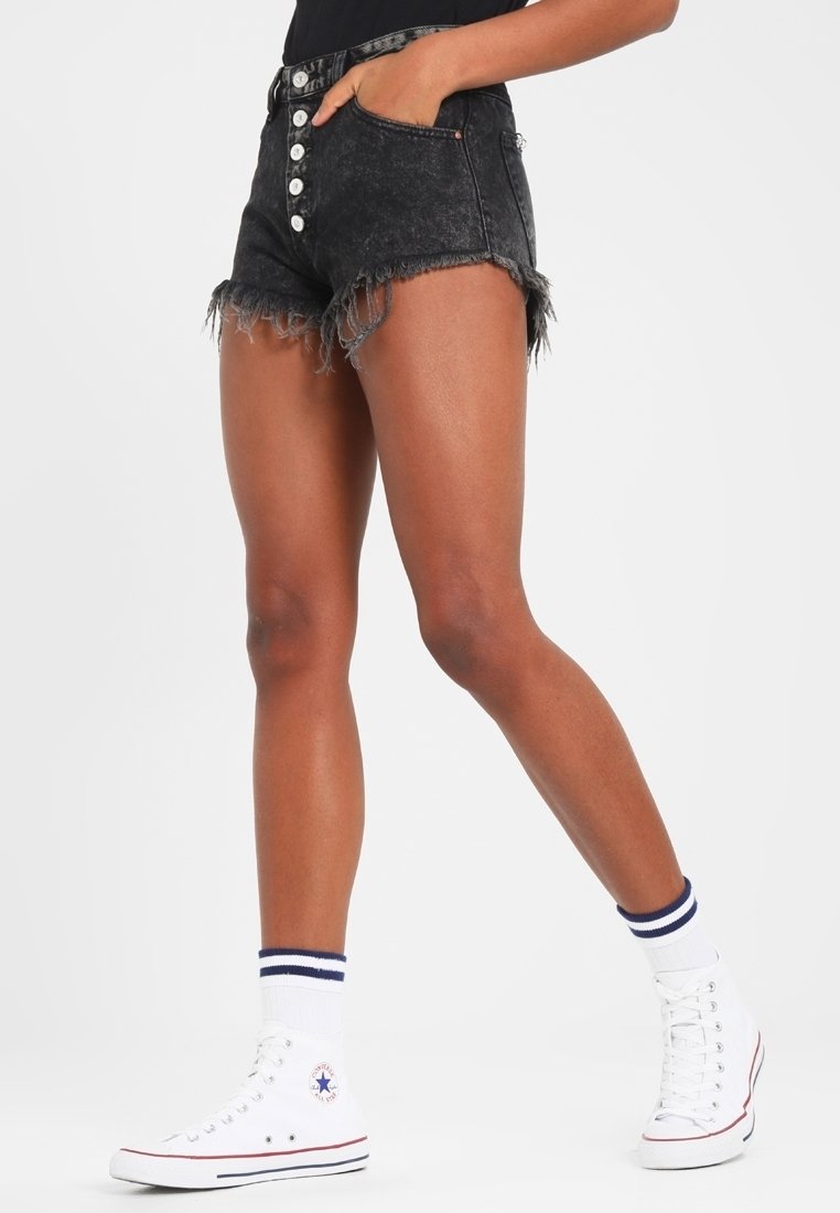 Mustat farkkushortsit, joissa on revitty helma, korkea vyötärö ja viisi nappia. Yhdistetty valkoisiin tennareihin ja raidallisiin nilkkasukkiin.