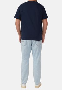Granatowa koszulka bawełniana z okrągłym dekoltem, krótkimi rękawami i luźnym krojem, zestawiona z jasnoniebieskimi dżinsami i białymi trampkami.