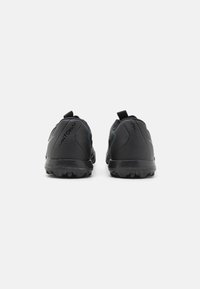 Des chaussures de sport noires avec une semelle en caoutchouc texturé, un talon rembourré et un logo de marque contrastant. Elles disposent de deux languettes pour un enfilage facile.