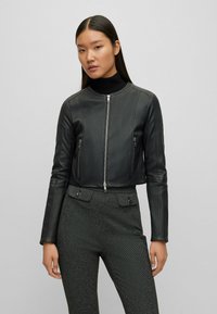 Svart läderjacka i croppad modell med dragkedja framtill, minimalistisk design och två fickor med dragkedja. Bärs med texturerade högmidjade byxor.