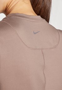 Brun träningsskjorta med sömlös design, slät textur och en subtil grå Nike-logga på baksidan av nackområdet.