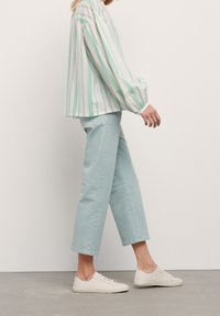 Femme marchant vêtue d'un chemisier rayé vert menthe, d'un pantalon court bleu clair et de baskets blanches sur fond blanc.
