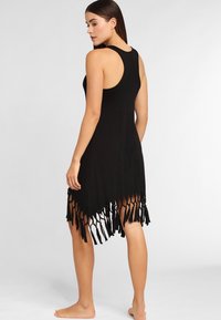 Vestido negro sin mangas con un dobladillo de flecos, hecho de un tejido suave. El diseño cuenta con un escote redondeado y un corte relajado.