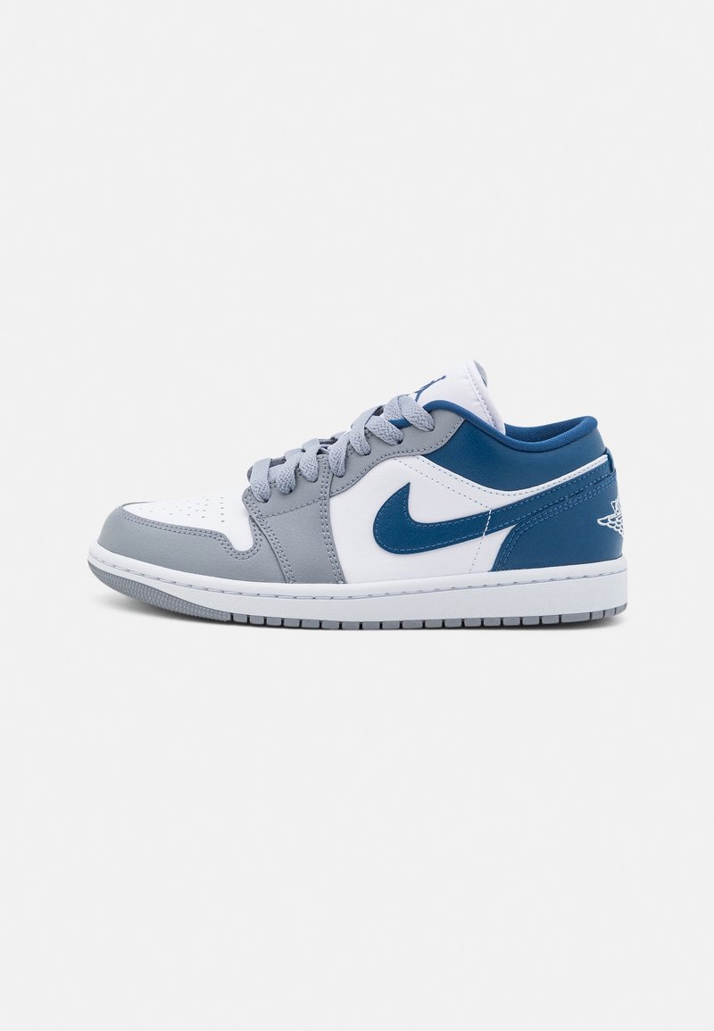 Baskets basses avec des panneaux gris, blancs et bleus, swoosh Nike bleu, lacets gris et semelle blanche, vues de côté sur fond gris.