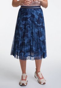 Jupe midi plissée au motif camouflage bleu, fabriquée en matériau transparent avec une taille texturée. Associée à des baskets chunky.