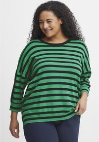 Zeleno-črno črtasta jopica s prostim krojem, okroglim izrezom in gumbnimi detajli na rokavih. Mehka pletenina s sproščenim oblikovanjem.