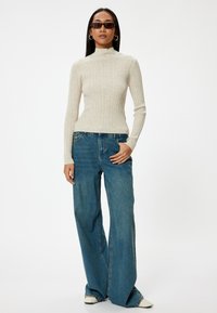 Beige geribbelde coltrui gecombineerd met wijde blauwe spijkerbroeken. De outfit heeft lange mouwen en een ontspannen pasvorm in denim.