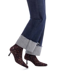 Botines estampados de leopardo hechos de un tejido suave, con punta afilada y tacón stiletto delgado, combinados con jeans oscuros de mezclilla remangados.