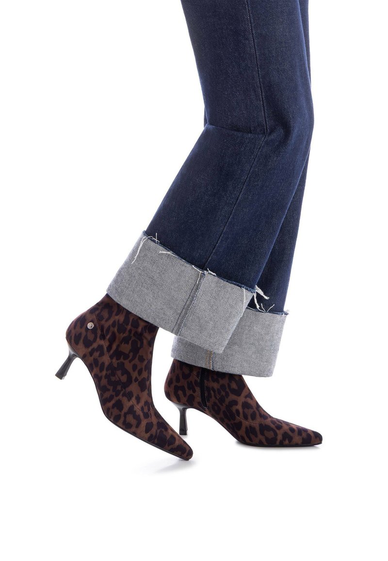 Botines estampados de leopardo hechos de un tejido suave, con punta afilada y tacón stiletto delgado, combinados con jeans oscuros de mezclilla remangados.