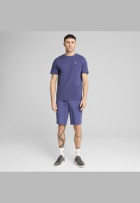 Lilla t-shirt med jersey stof og shorts sæt. Har et lille logo på brystet og på shortsene. Båret med grå sneakers og hvide sokker.
