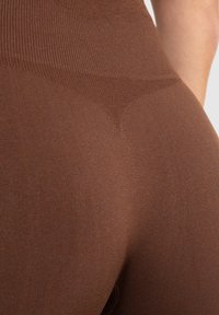 Bruine high-waisted legging gemaakt van een glad, rekbaar materiaal. Heeft een geribbelde textuur bij de tailleband en een gevormd ontwerp.