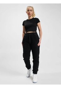 Svart avkortet t-skjorte med en jevn tekstur, kombinert med lodne svarte joggebukser med elastisk liv og sidelommer. Hvite sneakers.