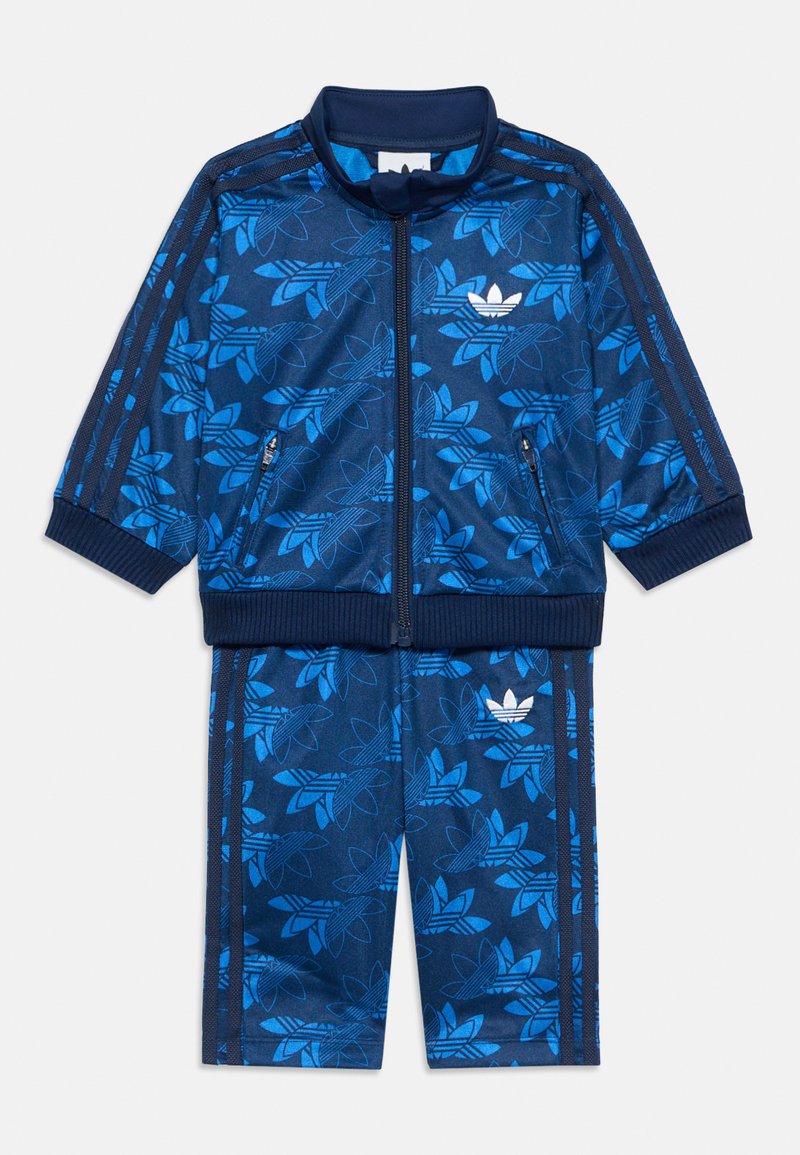 Blauwe Adidas trainingspak met een bloemenpatroon, een ritsjack en broek met elastische tailleband. Gemaakt van soepel stof met gestreepte accenten.