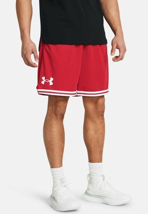 Mann trägt rote Under Armour Sportschorts mit weißen Streifen am Saum, weiße Knöchelsocken und weiße Turnschuhe, steht vor weißem Hintergrund.