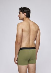 Olivgrüne Boxershorts mit einem schwarzen Bund, ausgestattet mit einem glatten, dehnbaren Stoff und einem enganliegenden Design, das die Körperform betont.