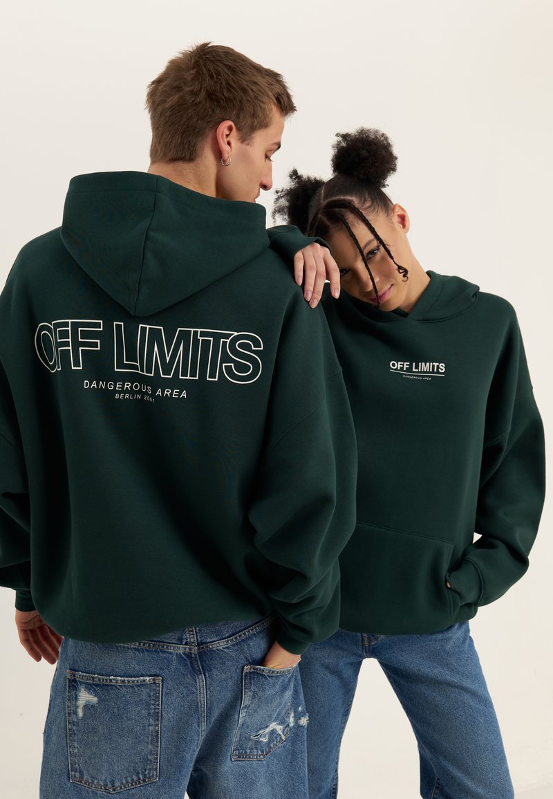 Dark green hoodies feature large white text reading "OFF LIMITS" on the back and front. Worn with light blue distressed jeans.