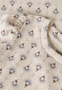 Miękka, kremowa bawełniana tkanina o prążkowanej strukturze, z kwiatowym wzorem w niebieskim i różowym kolorze, z brązowymi strzałkami, oraz okrągłym dekoltem.