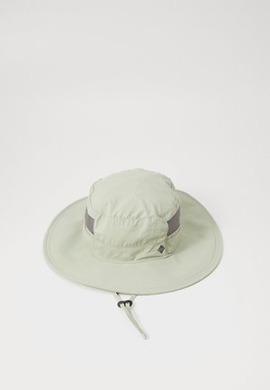 Gaiši zaļš ādas cepures formas vāciņš, izgatavots no mīksta auduma. Tam ir plata mala un sietiņa akcenti sānos. Iekļauts regulējams zoda siksna.