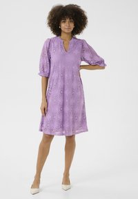 Lavandas krāsas mežģīņu kleita ar īsām puff piedurknēm, V veida kakla izgriezumu, ziedu rakstu un nedaudz paplatinātu svārku. Kvalitatīvi kombinēta ar nude stūrainas formas augstpapēžu kurpēm.