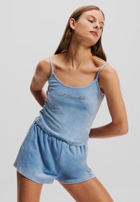Blue velour loungewear set featuring a sleeveless top with a rounded neckline and matching shorts with an elastic waistband. Subtle logo detail.