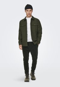 Olive green button-up jacket over a white shirt, paired with dark green corduroy pants and gray boots. Simple design, practical look.