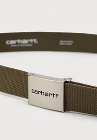 Olivno zelena tkanina pas s srebrnim pravokotnim kovinskim sponko, na kateri je vgraviran logotip "carhartt".