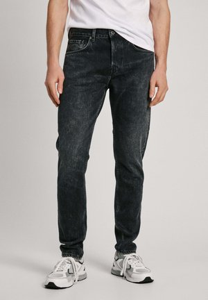 Slim-fit dark wash jeans made from denim, featuring a classic five-pocket design and subtle fading. Worn with white athletic shoes.