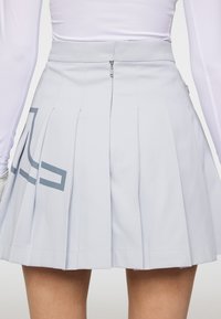 Jasnoszara plisowana spódnica z zapięciem na zamek z tyłu oraz kontrastowym geometrycznym wzorem po lewej stronie. Gładka tekstura.