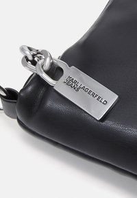 Svart läder crossbody-väska med en slät textur, med en stor silverkedja och en metalltavla präglad med "KARL LAGERFELD JEANS."
