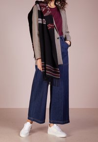 Grå och svart rutad kavaj, vinröd topp, vida blå denimbyxor och vita sneakers. Svart och röd mönstrad scarf som hänger över axlarna.