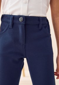Pantaloni blu navy realizzati in tessuto testurizzato con chiusura a bottone, passanti per cintura e tasche frontali, presentano gambe diritte e una finitura senza cuciture.