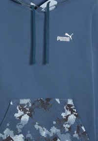 Puma hættetrøje i mørkeblå. Har en struktureret camouflage-mønstret lomme, kontrastfarvet hvidt logo og matchende snore.