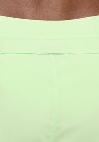 Gros plan de la taille arrière d’un pantalon vert clair porté par une personne à la peau foncée.