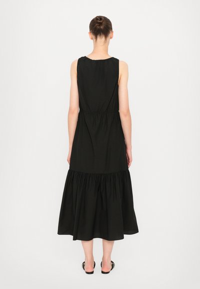 Black sleeveless dress with a gathered waist and tiered ruffle hem. Made from soft fabric, featuring a smooth texture and a flowing silhouette.